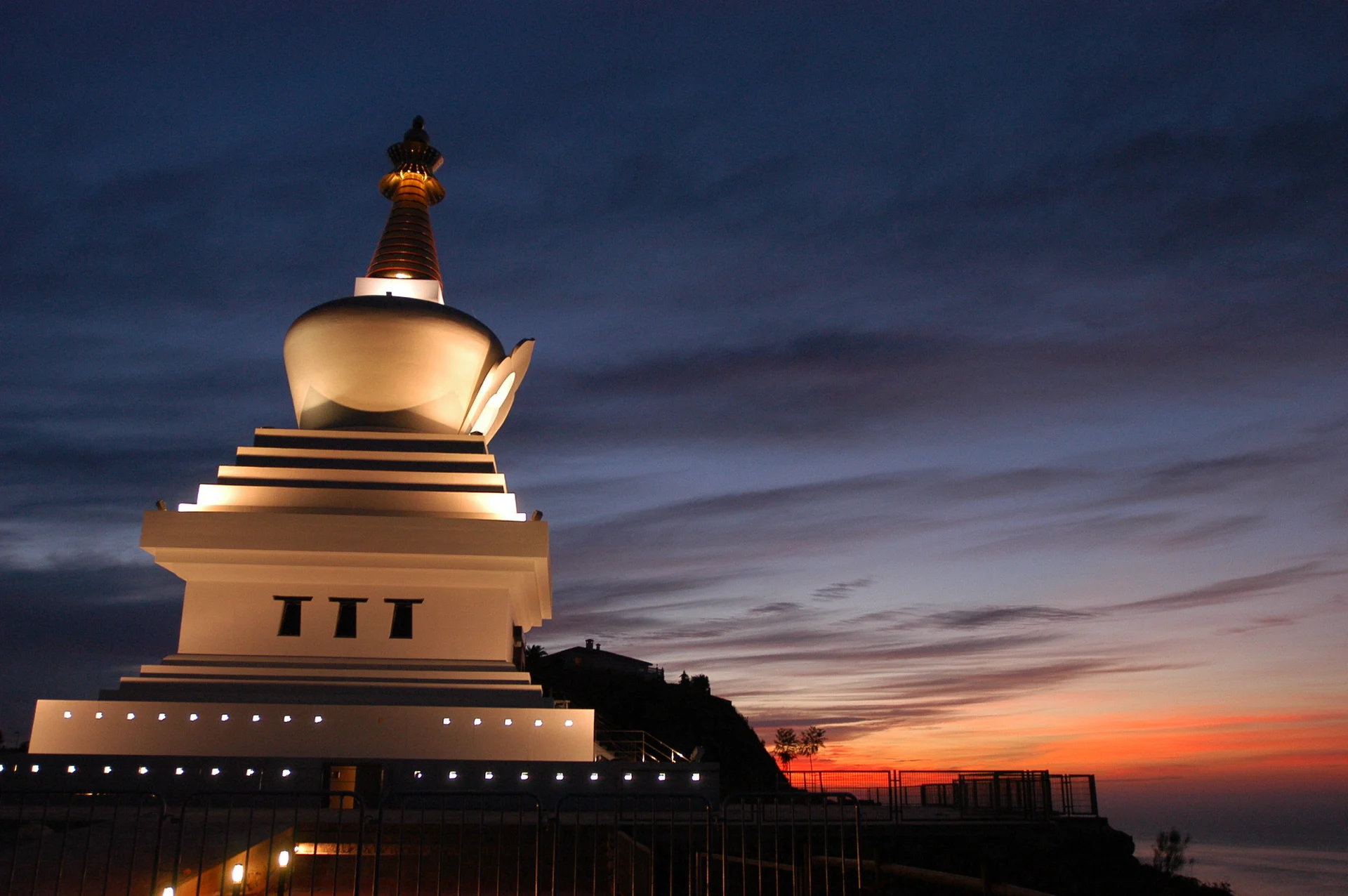 Illuminated Buddhist stupa at dusk above the sea